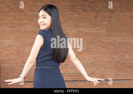 Selbstbewusst und Smart asiatische Frau mit rotem Backstein Wandinnenseite umdrehen Stockfoto