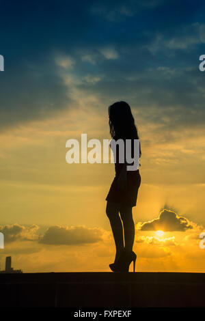 Volle Länge Frauen-Silhouette, die zu Fuß gegen einen dramatischen Sonnenuntergang