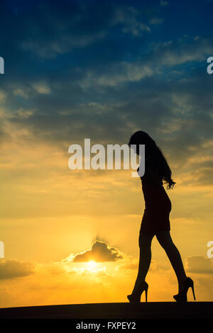 Volle Länge Frauen-Silhouette, die zu Fuß gegen einen dramatischen Sonnenuntergang