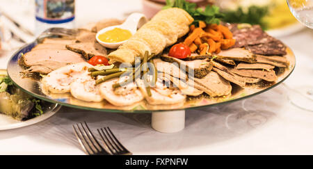 Platte mit in Scheiben geschnittenen Schinken, Salami und Wurstwaren mit Gemüse Dekoration auf festlich gedeckten Tisch. Stockfoto