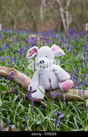 Des Kindes Stofftier Maus sitzen auf einem Baumstamm unter den Glockenblumen. Stockfoto