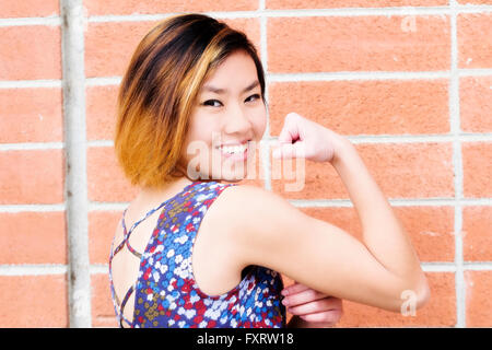 Lächelnd dünn asiatisch-amerikanische Frau zeigt Bizeps Stockfoto