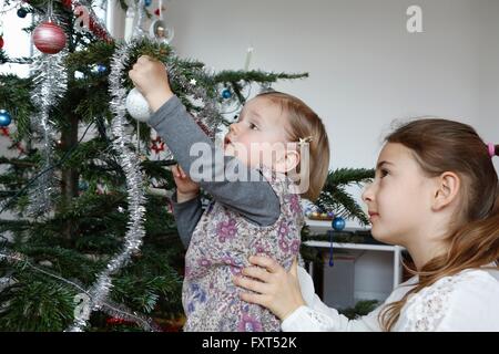 Seitenansicht der großen Schwester helfen Mädchen schmücken Weihnachtsbaum Stockfoto