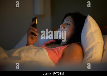 Reife Frau lesen Smartphone Texte im Hotelbett in der Nacht Stockfoto