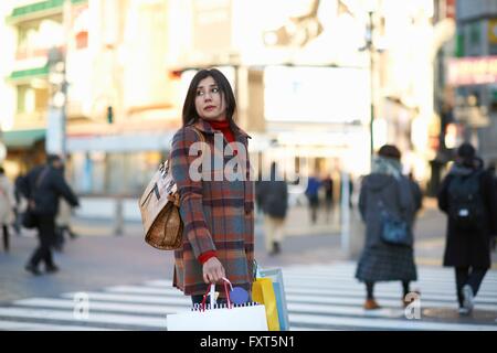 Seitenansicht des Reife Frau in Stadt Einkaufstaschen wegsehen über Schulter, Shibuya, Tokyo, Japan Stockfoto