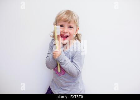 Mädchen halten große Zahnbürste, Blick in die Kamera Lächeln auf den Lippen Zunge herausragen Stockfoto