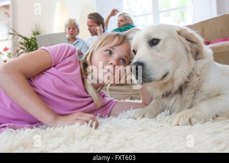 Mädchen und Haustier Hund liegend auf dem Teppich, Familie mit Laptop im Hintergrund Stockfoto