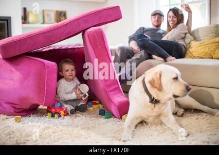 Baby Boy und Haustier Hund spielen im Fort aus Sofakissen hergestellt Stockfoto