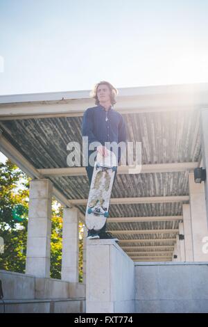 Portrait von junge männliche urban Skateboarder stehen auf Wand mit skateboard Stockfoto