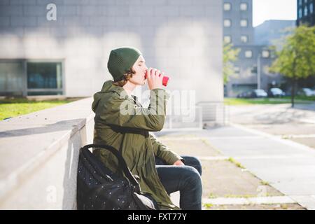 Junger Mann sitzt auf städtischen Wand aus trinken kann Stockfoto