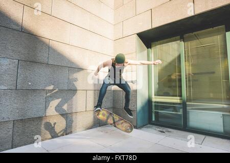 Junge männliche urban Skater tun Skateboard Sprung Trick in Ecke Stockfoto