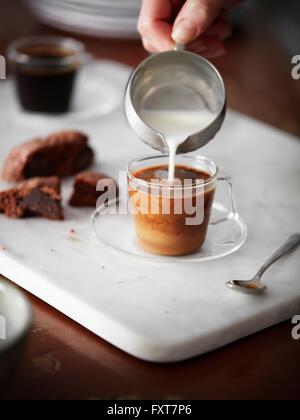 Womans hand Gießen Milch in Kaffee Stockfoto