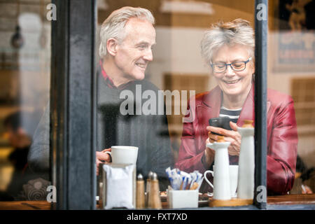 Älteres Paar im Café Fensterplatz, trinken Kaffee und SMS auf dem smartphone Stockfoto