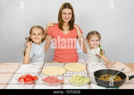 Mutter mit zwei Töchtern am Küchentisch gehen kochen eine Pizza und ein lustiges Aussehen in den Rahmen Stockfoto