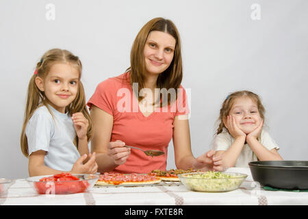 Mama mit zwei kleinen Mädchen sitzen am Küchentisch eine Pizza vorbereiten Stockfoto