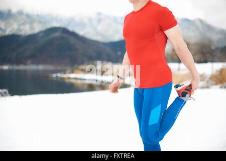 Seitenansicht des männlichen Läufer Dehnung Bein von Schnee bedeckt am See, Lake Kawaguchiko, Mount Fuji, Japan Stockfoto
