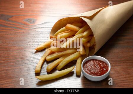 Erhöhte Ansicht von Chips in Papier-Membran mit Schüssel Tomaten-ketchup Stockfoto