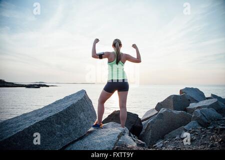 Rückansicht der Frau auf Felsen Arme angehoben biegen Muskeln Stockfoto