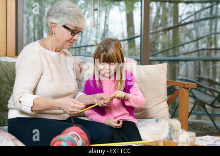 Ältere Frau unterrichtet Enkelin stricken auf Sofa im Wohnzimmer Stockfoto