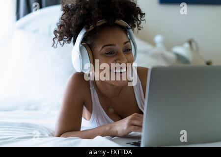 Frau im Schlafzimmer, mit Laptop, mit Kopfhörern Stockfoto