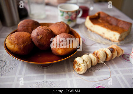 Hausgemachte Krapfen und Obwarzanki auch Käsekuchen auf dem Küchentisch liegend mit Wachstuch, große leckere Donuts auf Platte. Stockfoto