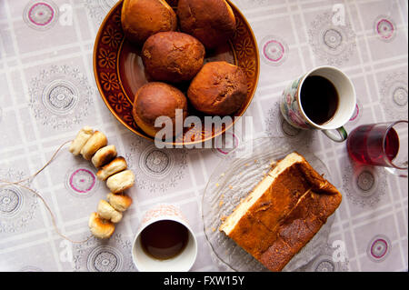 Hausgemachte Mehlspeisen, Krapfen, Obwarzanki und Käsekuchen auch Tee in Tassen auf dem Küchentisch mit Wachstuch, leckeres Essen. Stockfoto