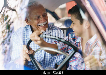 Familie und die Kluft zwischen den Generationen. Alte Opa verbringen Zeit mit seinem Enkel und unterrichtete ihn zu fahren. Der junge hält die Volante von einem Stockfoto