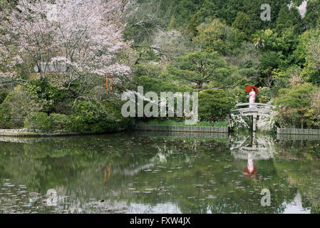 Japanische Frau im Kimono mit roten Wakasa Regenschirm auf Brücke an Ryōan-Ji Zen-Tempel beherbergt berühmte Steingarten, Kyoto, Japan Stockfoto