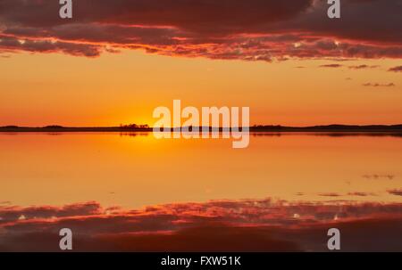 Orange und rote Himmel nach Sonnenuntergang an einem See in Finnland. Symmetrische Reflexion der Wolken in das Stille Wasser. Stockfoto