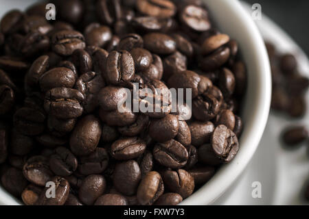 Kaffeetasse überfüllt mit Kaffeebohnen, geringe Schärfentiefe Stockfoto