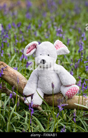 Des Kindes Stofftier Maus sitzen auf einem Baumstamm unter den Glockenblumen. Stockfoto