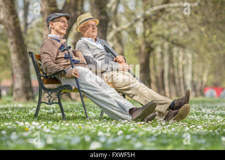 Zwei ältere Herren sitzen und entspannen auf einer Holzbank in einem Park an einem sonnigen Tag Stockfoto