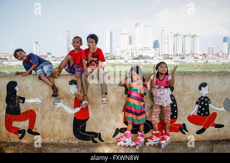 Jakarta, Indonesien. 18. April 2016. Kinder spielen am Flussufer wie Hochhäuser auf dem Hintergrund gesehen werden. © Garry Andrew Lotulung/Pacific Press/Alamy Live-Nachrichten Stockfoto