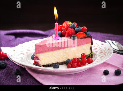 Portion leckeren Himbeer-Käsekuchen mit frischen Beeren, Schokolade und Kerzen dekoriert Stockfoto