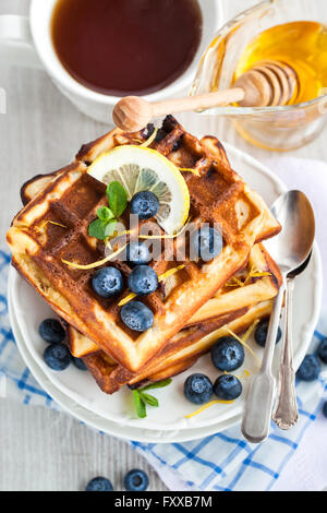 Zitrone Blaubeere Waffeln mit Honig, Zitronenschale, frische Beeren und Tee Stockfoto