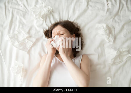 Young, deprimiert oder krank mit Grippe-Modell auf dem Bett liegend mit geschlossenen Augen und ihre Nase in das Gewebe. Stockfoto