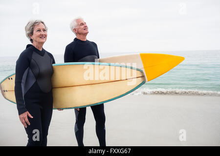 Älteres Paar mit Surfbrett stehend am Strand Stockfoto