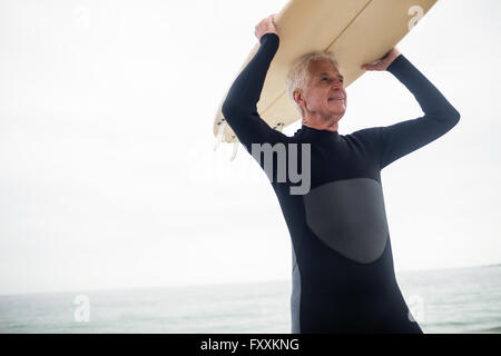 Senior woman ein Surfbrett über den Kopf halten Stockfoto