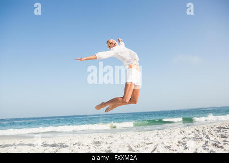 Blonde Frau springen am Strand Stockfoto
