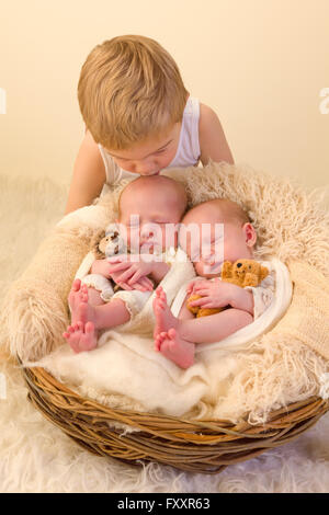 Kleinkind Jungen posiert mit seinem Neugeborenen eineiigen Zwillings-Schwestern Stockfoto