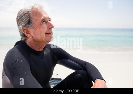 Happy senior woman im Neoprenanzug sitzt am Strand Stockfoto