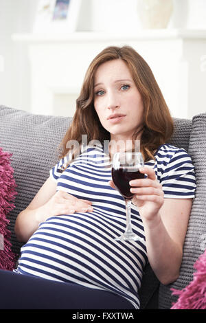 Betroffene schwangere Frau zu Hause Trinkglas Rotwein Stockfoto