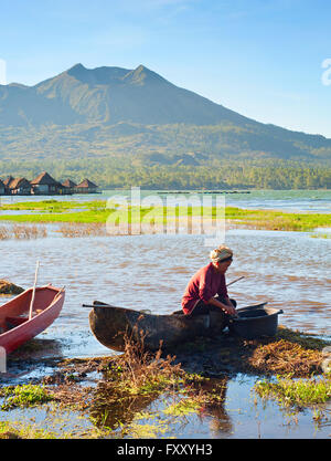 Balinesische Frau Reinigung Fische im traditionellen Boot in einem Kratersee, Batur Vulkan im Hintergrund Stockfoto