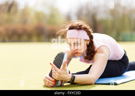 Sportliche Mädchen tun stretching auf Fitness-Matte. Attraktive Sportlerin, die Dehnung in der Natur Stockfoto