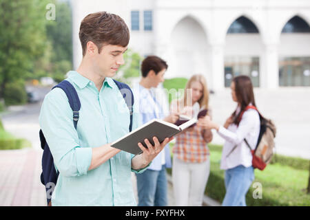 Internationale Schüler in der Schule mit einem Buch vor dem Hintergrund seiner Freunde zusammen auf dem Campus Rucksack Stockfoto