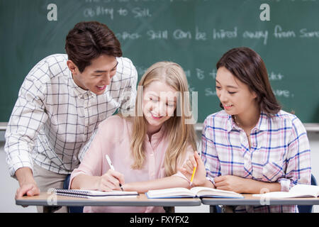 Zwei einheimische Studierende, die einen internationalen Student mit dem Studium in einem Klassenzimmer in der Schule helfen Stockfoto