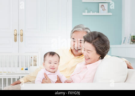 Großeltern, die Betreuung eines Kindes auf einer Couch alle lächelnd Stockfoto