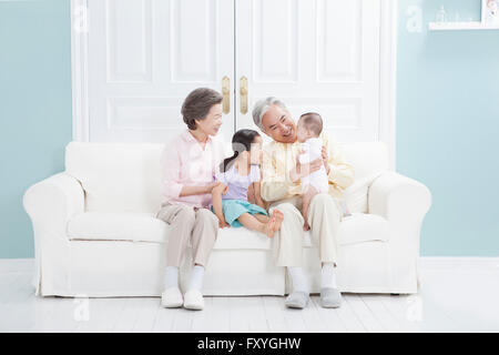 Enkelin und ein Baby bei den Großeltern auf einem Sofa sitzend Stockfoto