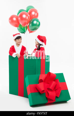 Lächelnde junge und Gril in Santas Kleidung in eine große Geschenkbox von Angesicht zu Angesicht Ballons Stockfoto