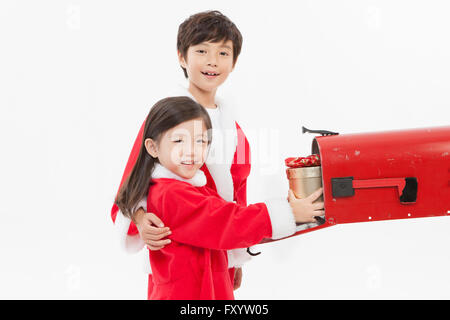 Seite Ansicht Porträt von lächelnden jungen und Gril in Sata Kleidung platzieren eine Geschenkbox in einen Briefkasten starrte auf Vorderseite Stockfoto